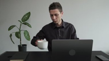 İçişleri Bakanlığı 'ndaki bir bardaktan kahvesini yudumlayan adam bilgisayarlı bir masanın arkasında. Freelancer rutini. Gün ışığı, ev içi..