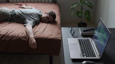 Yorgun ve serbest çalışan biri yatağa uzanır ve çalışmaya devam edemez. Dizüstü bilgisayar ve gözlük masada dinleniyor. Ev ofis ortamında serbest çalışmanın, iş hayatında dengesizliğin ve duygusal yorgunluğun gerçekçi bir tasviri..