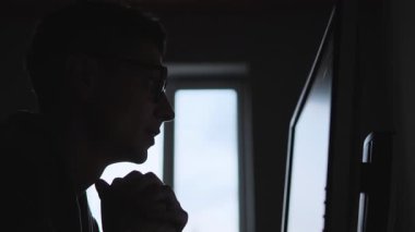 Gözlüklü adam, yatırımlarını, kripto veya borsa çöküşünü, yalnızlığı ve finansal stresi yansıtan loş ışık altında, hayal kırıklığına uğramış bir ifadeyle monitörün önünde oturuyor.