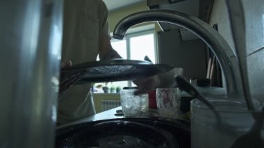 Tabakları bulaşık deterjanı ve süngerle temizleyen eller. Dağınık tabaklarla gerçekçi mutfak temizliği.