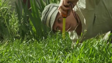 Genç adam çimlerin detaylı ölçümünü yapıyor, komik ve ironik bahçe sahnesi.