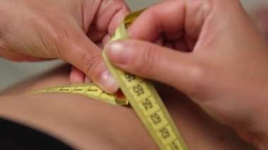 Vücut kontrolü sırasında kadın ellerinin çıplak deride sarı mezura ile ölçülen bel ölçüleri yakın plan.