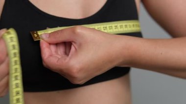 Göğüs ölçülerini ölçmek için siyah spor sutyeninin üzerine sarı bant takılmış kadın ellerinin yakın çekimi.