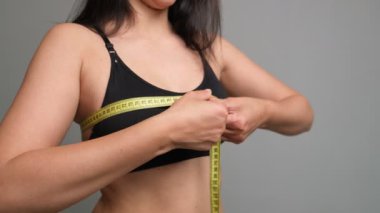 Genç bir kadın aynadaki bantla büstü ölçüyor. İç çamaşırlı kişisel sağlık kontrolü, doğal sahne..