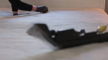 Profesyonel temizlikçi eldiven giyerek yatak odasındaki yatağı sterilize ediyor. Ön planda görülen sprey çıkarma makinesini kullanıyor.