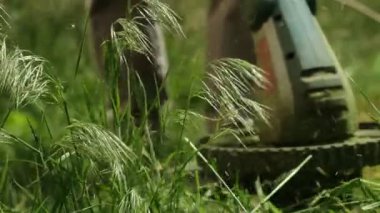 Çimleri yavaş çekimde kesen elektrikli budayıcının yakın çekimi. Uçan ot parçalarıyla dinamik bir sahne