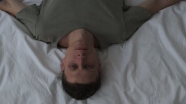 Depresyon geçiren bir erkek. Yatakta tek başına yatan bir adam, tavana yakından bakıyor. Üst görünüm.