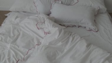 Yatak odasında beyaz çarşaflı ve yumuşak battaniyeli yapılmamış yatak.