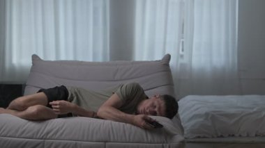 Yorgun adam elinde telefonuyla uyuyakalıyor. Dijital aşırı yükleme ve sabit ekran süresi onu tüketiyor.