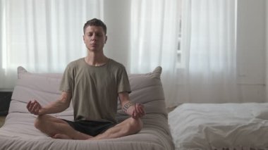 Genç adam modern koltukta gözleri kapalı meditasyon yapıyor. Minimalist iç mekanda iç huzuru buluyor..