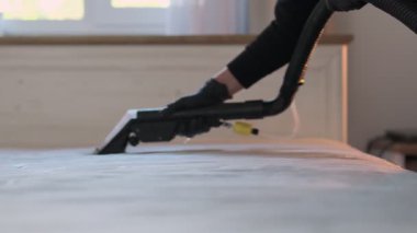 Yatak temizleme servisi. Siyah eldivenler giyerek temiz yatak yüzeyi oluşturmak için elektrikli süpürge kullanan profesyonel bir kadın..