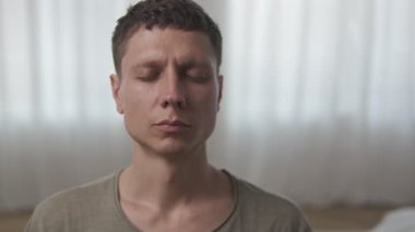 Genç adam modern koltukta gözleri kapalı meditasyon yapıyor. Minimalist iç mekanda iç huzuru buluyor..