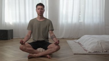 Dikkatli sabah rutini. Parlak minimalist yatak odasında meditasyon yapan genç adam..