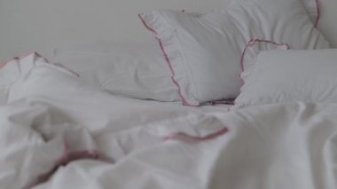 Yatak odasında beyaz çarşaflı ve yumuşak battaniyeli yapılmamış yatak.