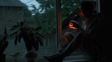 Yağmurlu bir akşamda kibritle esrar yakan genç bir adam, pencerenin kenarında dinleniyor..