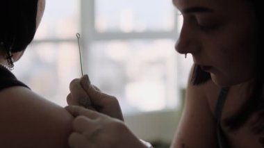 Genç bir kadın el dürtme dövmesi yapıyor, yavaş ve odaklı geleneksel sopa ve dürtme tekniği.