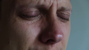 Close-up shot of a young man crying, eyes closed, showing intense emotion and vulnerability. His facial expression reflects deep sadness or emotional pain.