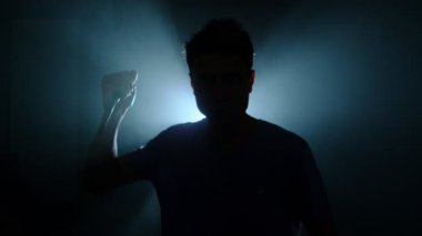 Karanlıkta elinde bıçakla duran genç adamın silueti. Tehlikeli bir suçlu, keskin bir silahı içeride elinde tutuyor. Soyguncunun arka planda hançer sallaması.