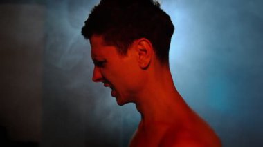 Duygusal çöküntü ve iç çatışma. Profildeki adam duman dolu dramatik sahnede kırmızı ve mavi ışıklarla aydınlatılıyor.