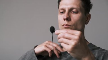 Adamın kıyafetlerine lavalier mikrofon taktığına yakın çekim. Bir podcast veya vlog için bir röportaj kaydetmeye hazırlanılıyor