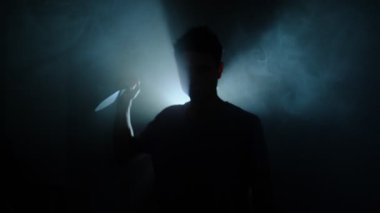 Mavi arka plan ışığı altında elinde bıçakla yaklaşan bir adamın silueti sinematik tehlike ve belirsizlik konsepti.