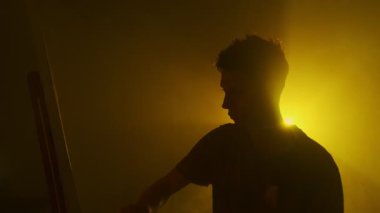 Sinema renkli ışıklandırma ve atmosferik dumanla karamsar stüdyoda resim yapan genç bir sanatçı.