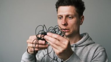 Genç bir erkek içerik yaratıcısı, kablolu bir mikrofonu çözmeye çalışır, sonra da mutlu bir şekilde bluetooth mikrofonuna geçer. Yüzü rahatlama ve sevinçle parlıyor. Modern kablosuz ses cihazlarının rahatlığını ve rahatlığını açıkça gösteriyor..