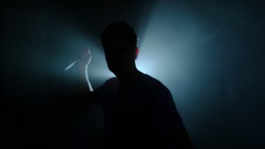 Mavi arka plan ışığı altında elinde bıçakla yaklaşan bir adamın silueti sinematik tehlike ve belirsizlik konsepti.