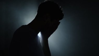 Karanlık odada, arka planda düşünen ve cevap arayan bir adamın silueti. Karanlık oda siluetinde bir adam elleri arkada. Ruhun karanlık gecesini sembolize ediyor.