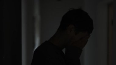 Karanlık koridorda elleri ve yüzü kaplayan genç adamın silueti kalp kırıklığını hissediyor..