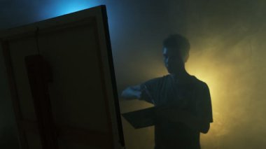Yaratıcı akışa kapılmış genç sanatçı, karamsar sinematik aydınlatma ve yavaş çekimde resim yapıyor.