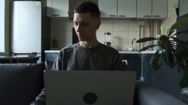 Dizüstü bilgisayarla çalışan serbest çalışan ve mutfak koltuğunda otururken telefonla proje mesajı gönderen serbest çalışan gerçek bir ofis sahnesi. Otantik uzaktan çalışma yaşam biçimi