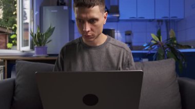 Gerçek hayatta ev ofis sahnesi. Sıradan kıyafetlerle serbest çalışan biri. Mutfakta, kanepede dizüstü bilgisayarda çalışıyor. Otantik uzaktan çalışma yaşam biçimi