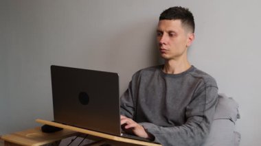 Gri kapüşonlu genç adam laptopunu kapatıyor ve bir gülümsemeyle esniyor. İşi ya da bir projeyi tamamladıktan sonra tatmin oluyor. Serbest çalışma, uzaktan çalışma, çevrimiçi işler, üretkenlik ve evde iş hayatı dengesi kavramı.