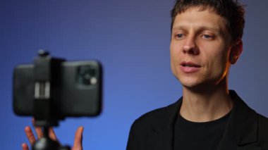 Takım elbiseli genç adam, RGB ışıklandırmalı arka plan uzaktan iletişim konseptiyle akıllı telefondan online video görüşmesi yapıyor..