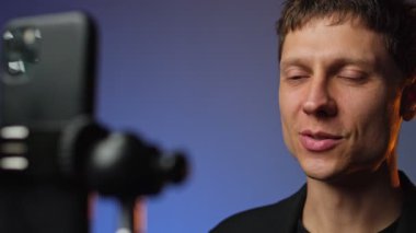 Takım elbiseli genç adam akıllı telefondan sosyal medya içeriğini kaydediyor rgb renkli arka plan stili modern kurulum.