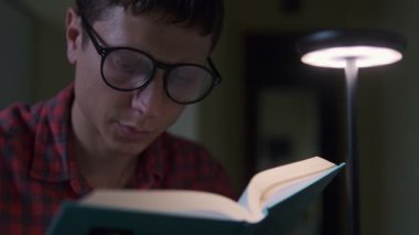 Masa lambası altında kitap okuyan odaklanmış genç adam, eğitim konsepti, evde öğrenim ve öğrenim yaşam tarzı.
