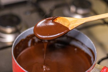 Wooden spoon stirring melting dark chocolate over a red pan