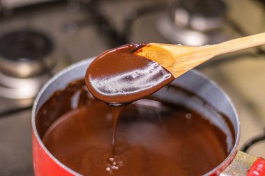 Wooden spoon stirring melting dark chocolate over a red pan