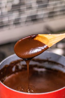 Wooden spoon stirring melting dark chocolate over a red pan
