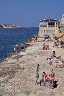 Valetta, Malta - 11 Haziran 2023: Malta Valetta şehrinin Rocky kıyı şeridi. Banyo yapan insanlar.