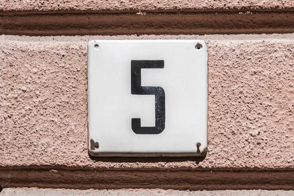 Old vintage minimalist street adress number sign with number 5 on the facade of the facade house wall.