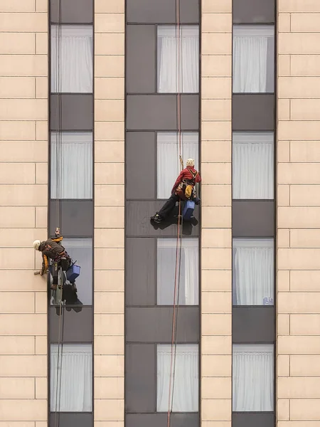 Two climbers wash windows on the facade of a modern building.