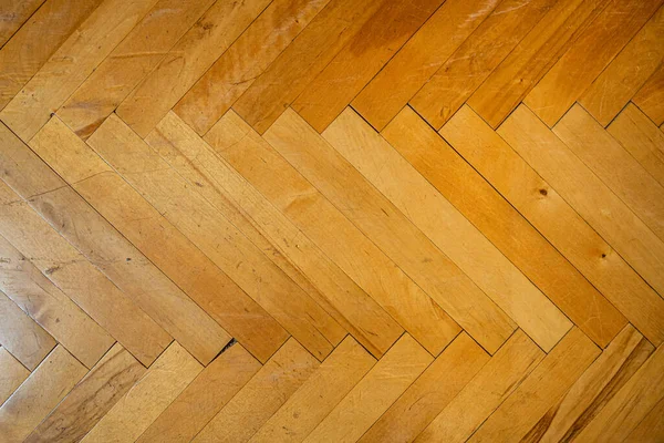 Texture of obsolete lacquered wood parquet laid out in the shape of a herringbone, close-up.