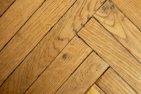 Texture of obsolete scratched lacquered wood parquet laid out in the shape of a herringbone, close-up.