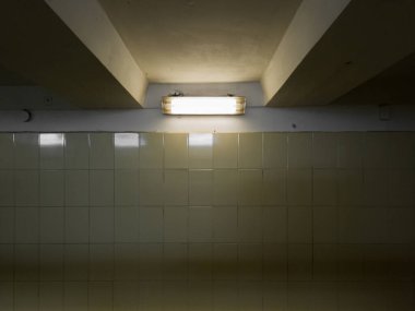 Duvarları bej renkli parlak fayanslarla kaplı karanlık bir yeraltı geçidinde bir lamba..