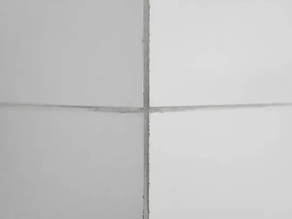 The corner of the wall is lined with white glossy ceramic tiles with gray grout between the tiles.