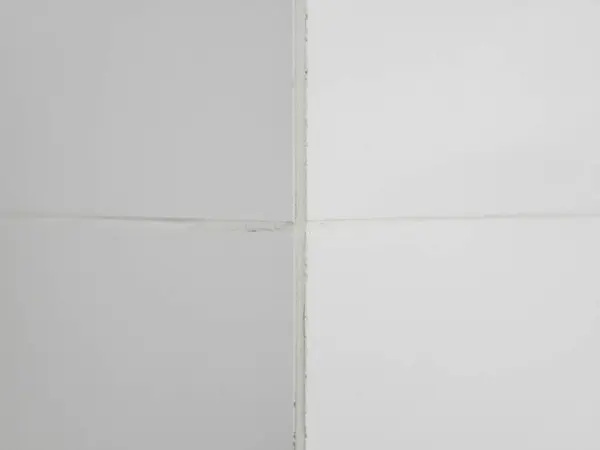 The corner of the wall is lined with white glossy ceramic tiles with white grout between the tiles.