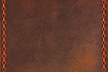 Kahverengi deri yüzey, dikey kenarlar ve telif boşluğu boyunca dikilmiş. Deri desenli, yıpranmış bir görünüme sahip, ve dikişler düzgün ve kumaşın işçiliğini ön plana çıkarıyor..