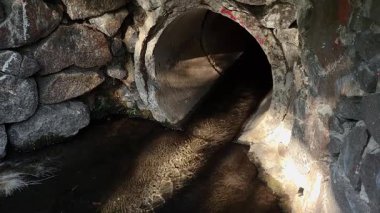 Eski yeraltı drenaj boruları su ve taş duvarlardan yansıyan güneş ışığıyla yüzeye çıkıyor..